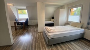 Un dormitorio con cama, escritorio y silla. Se ve una ventana con persianas, un armario y una lámpara en el techo.