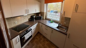 Eine kleine Küche mit weißen Schränken, einem Einbauofen, einer Mikrowelle und einer Kaffeemaschine.