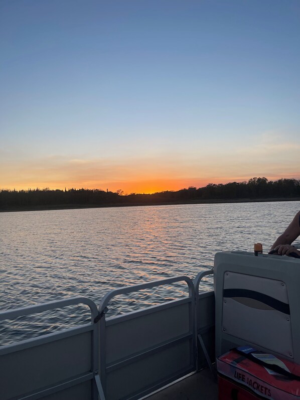 Un bote con una persona al timón, un chaleco salvavidas y un atardecer sobre el agua.