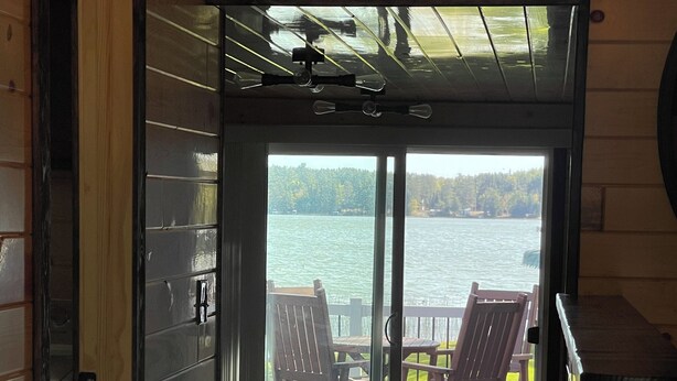 A wooden interior leading to a deck with two wooden chairs and a table, overlooking a body of water. - Lake cabin 2-bedroom sleeps 6.  1/2 mile from trails.  Backus with private dock. (Backus)