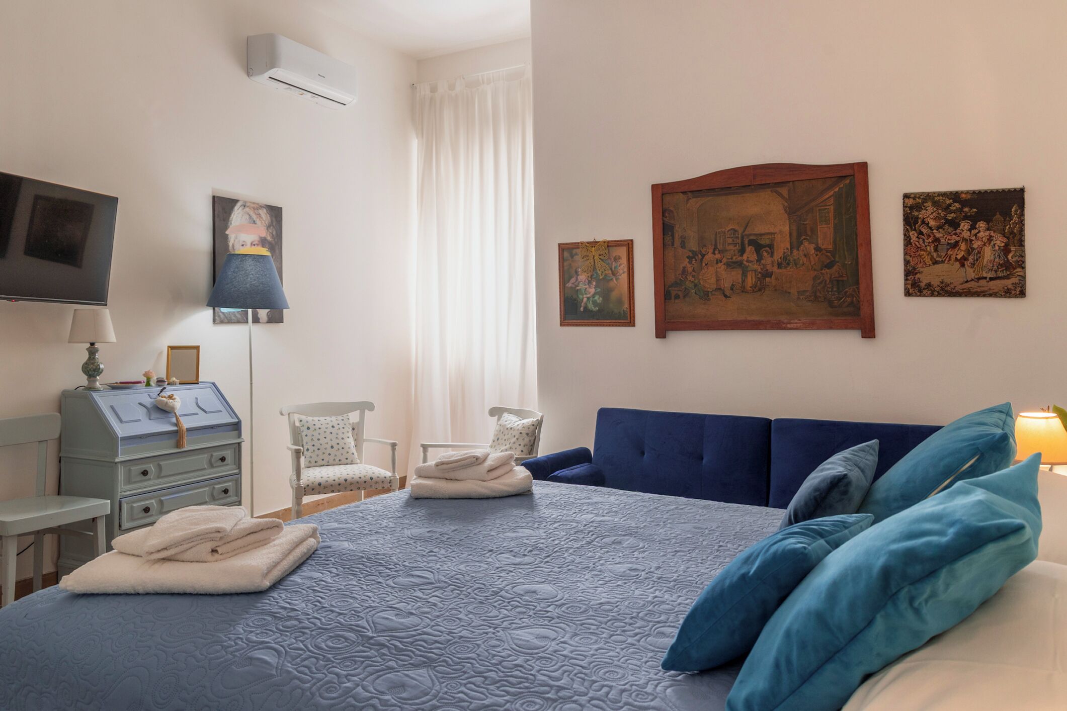 Un dormitorio ordenado con cama, una silla, un escritorio y un televisor.