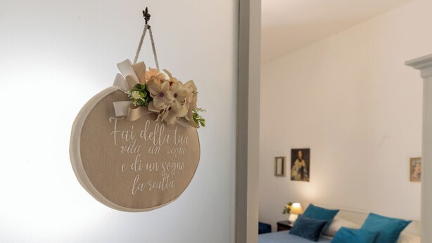 Ein rundes Schild mit italienischem Text, ein Bett mit blauer Bettwäsche und ein Nachttisch mit einer Lampe.
