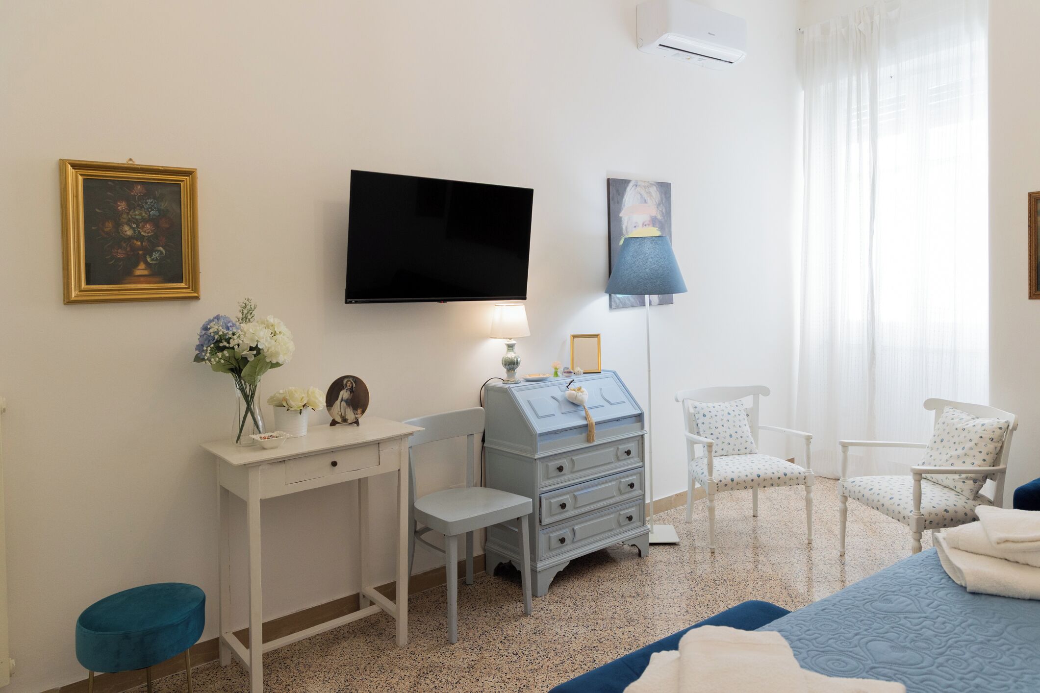 Een slaapkamer met een bed, een bureau, een stoel, een dressoir, een televisie en een raam met gordijnen.