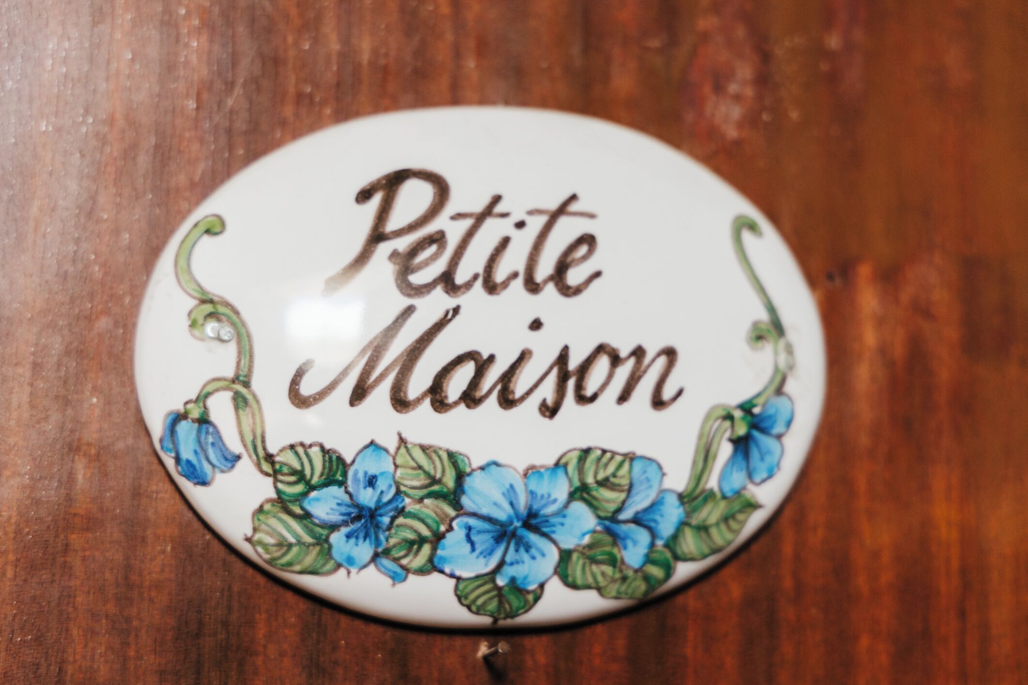 Un letrero ovalado con el texto 'Petite Maison' y diseños florales.