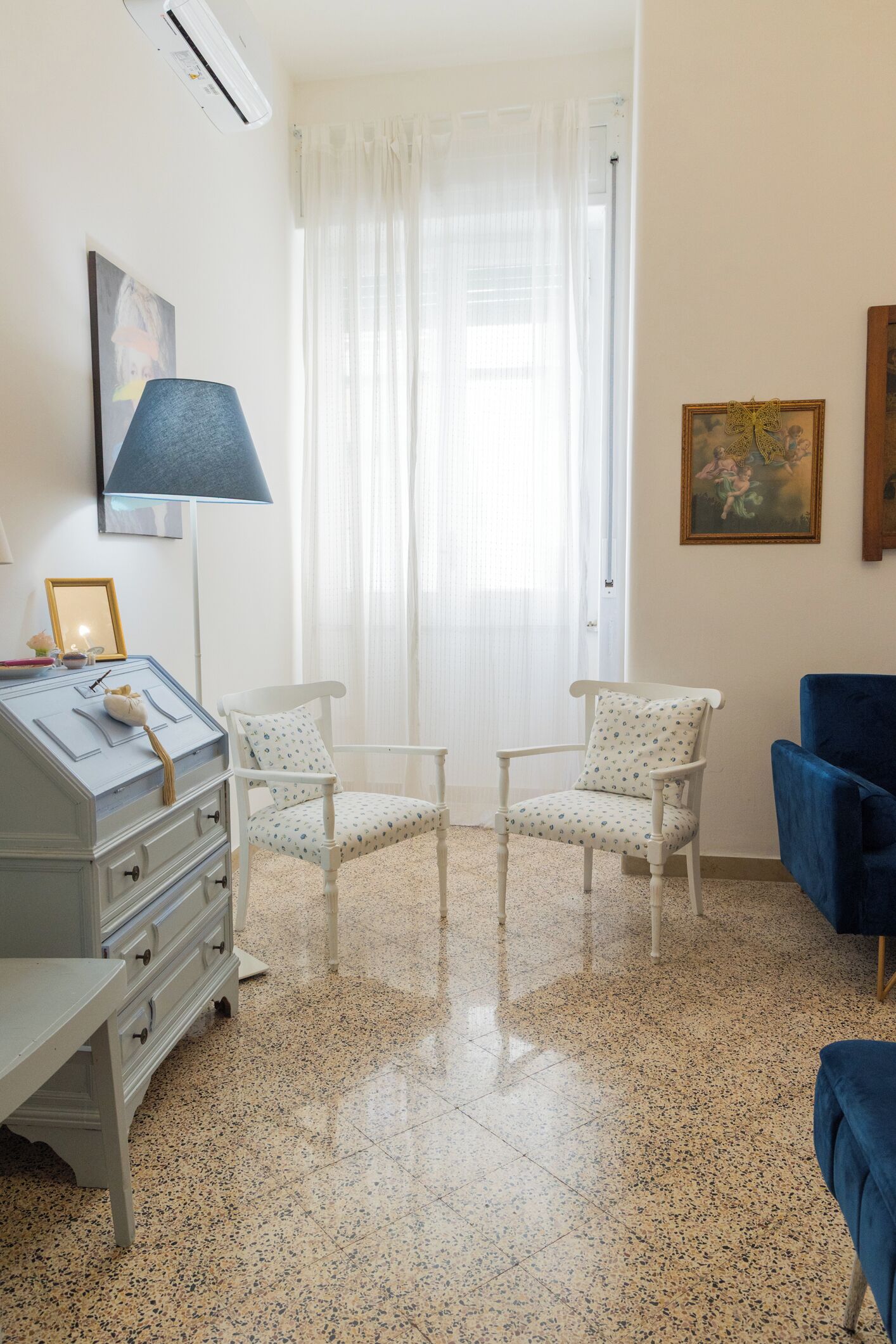 A room with a desk, two chairs, a lamp, and a window with curtains.