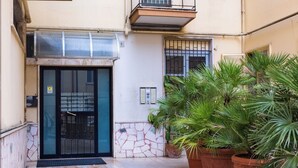 Une entrée d’immeuble avec une porte en verre, un portail en métal et des plantes en pot.