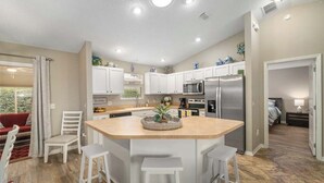 Uma cozinha moderna com armários brancos, uma ilha central com banquetas, uma geladeira e um micro-ondas.