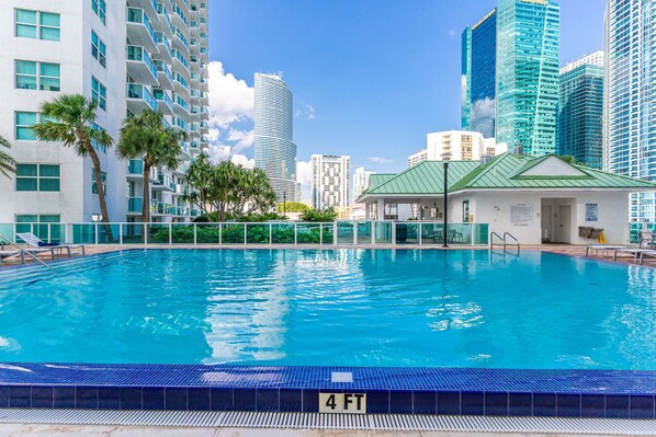A swimming pool with a 4 FT depth marker, surrounded by tall buildings and palm trees.