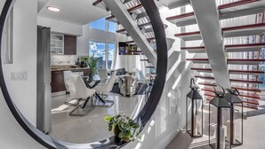 Un intérieur moderne avec un grand miroir rond qui reflète un escalier, un coin repas et une cuisine.