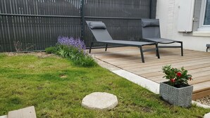 Eine Terrasse mit zwei Liegestühlen, einer Steinfläche und einem Pflanzgefäß mit roten Blüten.