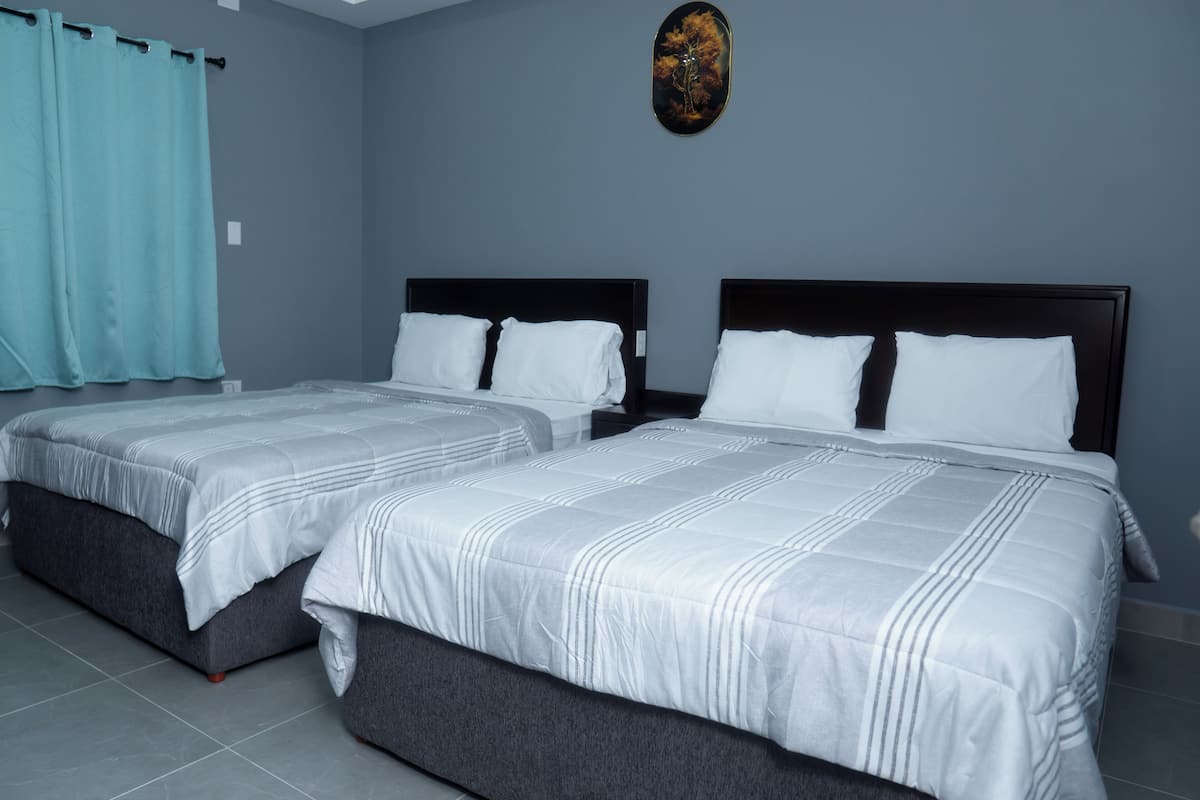 A hotel room with two beds, grey walls, and a blue curtain.