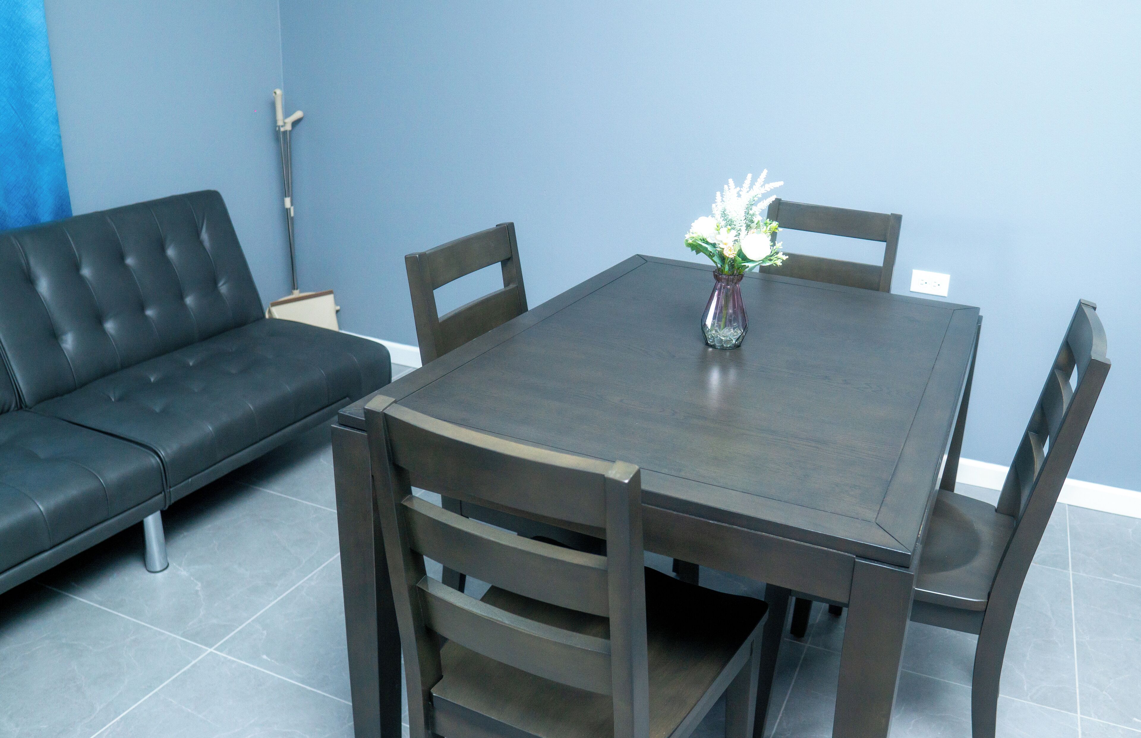 Un coin repas avec une table en bois foncé et quatre chaises, un vase rempli de fleurs et un canapé en cuir noir.