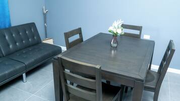 Un coin repas avec une table en bois foncé et quatre chaises, un vase rempli de fleurs et un canapé en cuir noir.