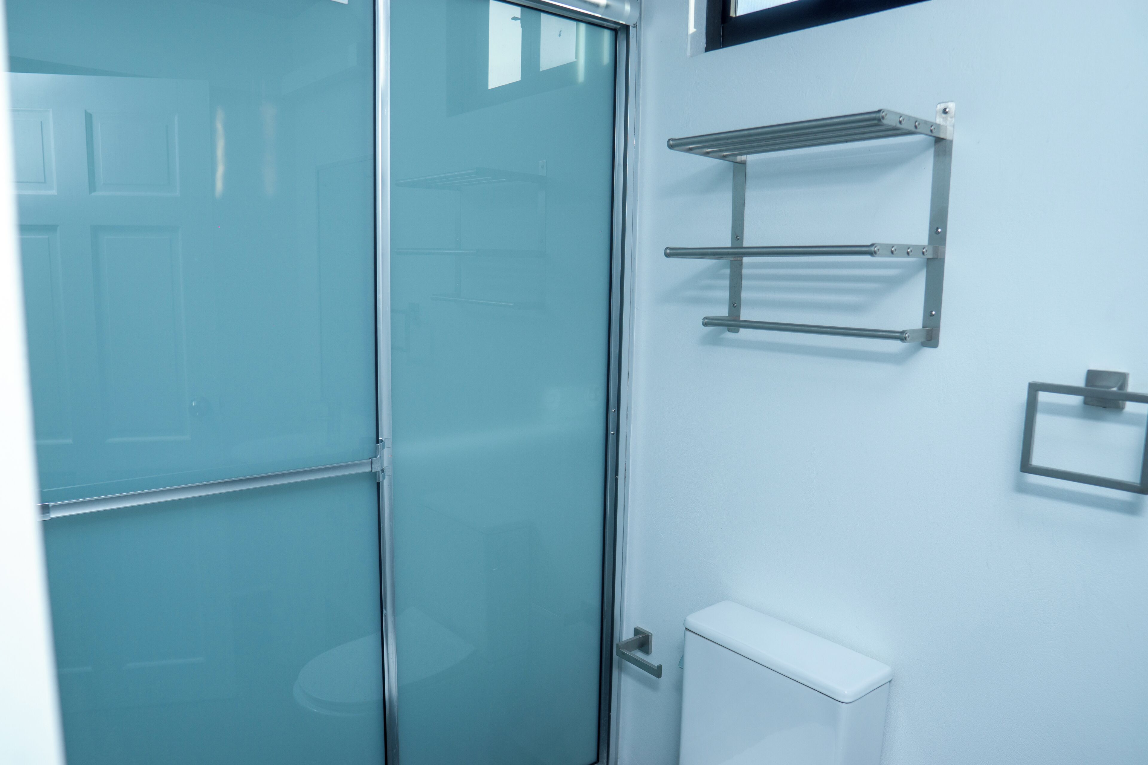 Un baño con cabina de ducha de vidrio, un inodoro blanco y un toallero metálico en la pared.