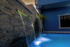 A stone wall with a water feature cascading into a pool. - The Blue Mirage (San Juan)