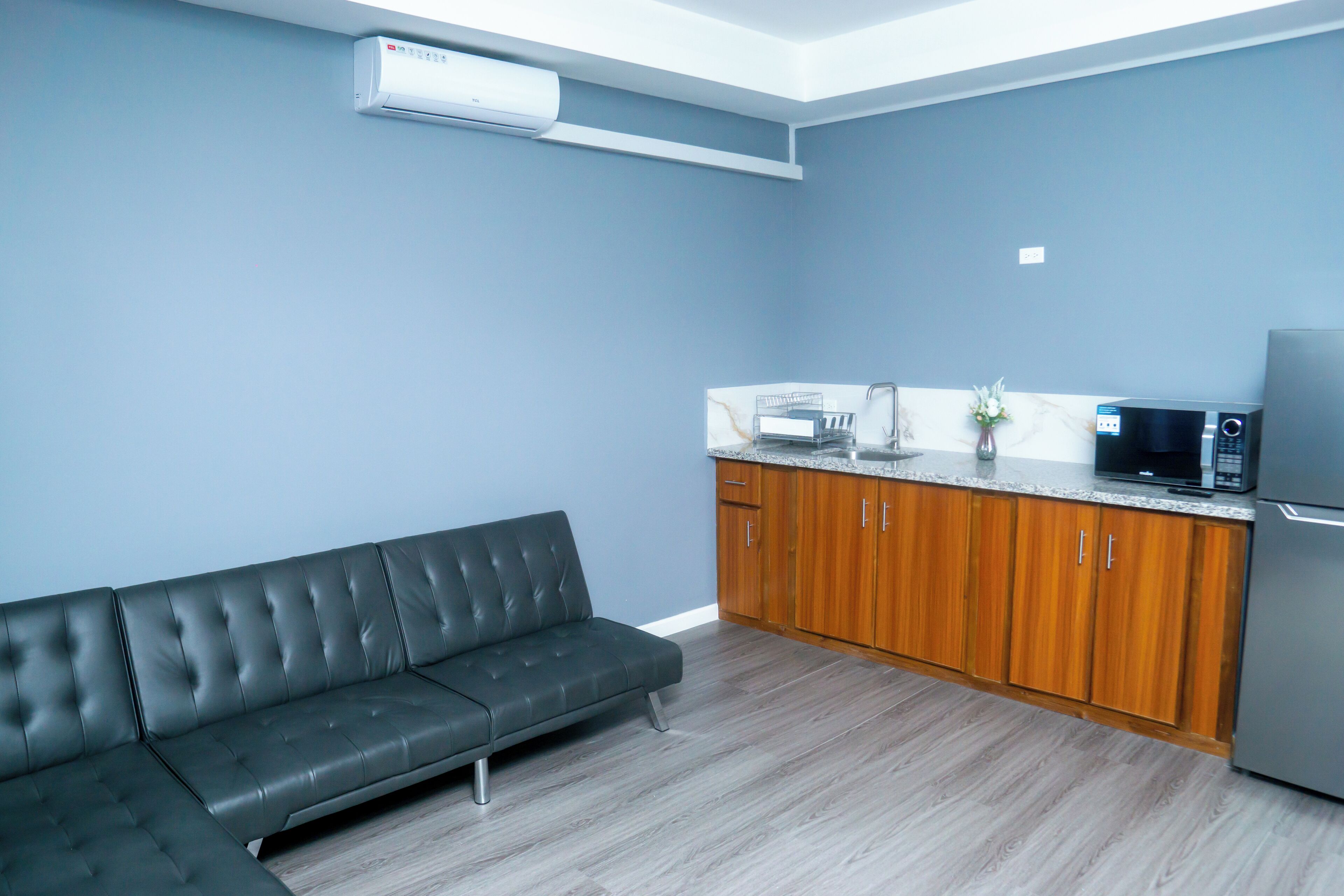 A modern kitchen with a grey sofa, wooden cabinets, and a built-in microwave.
