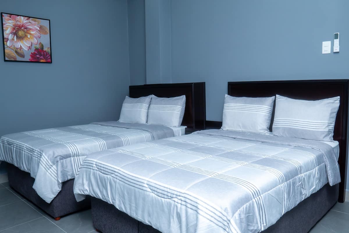 A hotel room with two beds, a large floral artwork on the wall, and a small table with a phone and papers.