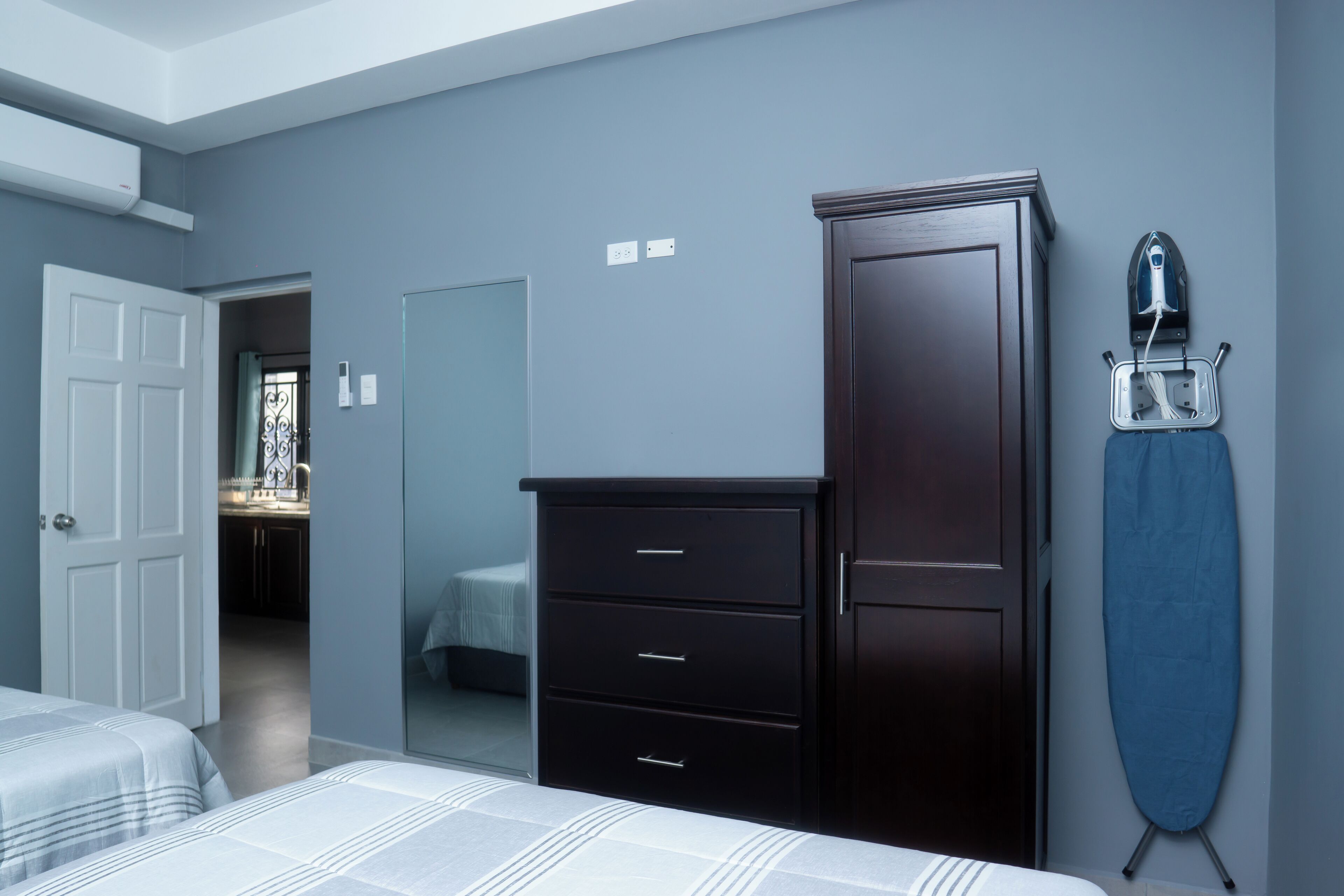 A bedroom with a bed, a dresser, a mirror, and an ironing board.