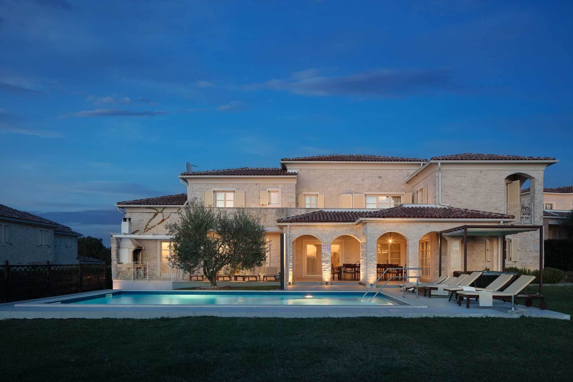 A two-story house with a swimming pool, outdoor seating, and a well-maintained lawn.