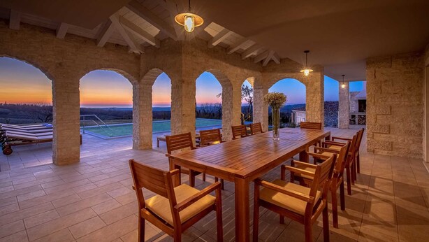 A spacious outdoor dining area with a long wooden table and chairs, surrounded by stone arches, and overlooking a scenic landscape during sunset. - Villa Sara Bajkini with vineyard view (Bajkini)