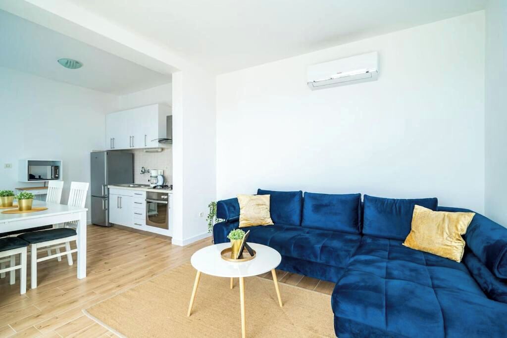 A modern living room with a blue sofa, white dining table, and a small round coffee table.