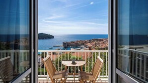 Un balcon avec deux chaises en bois et une petite table, d’où l’on peut admirer une ville côtière, un fort historique et la mer.