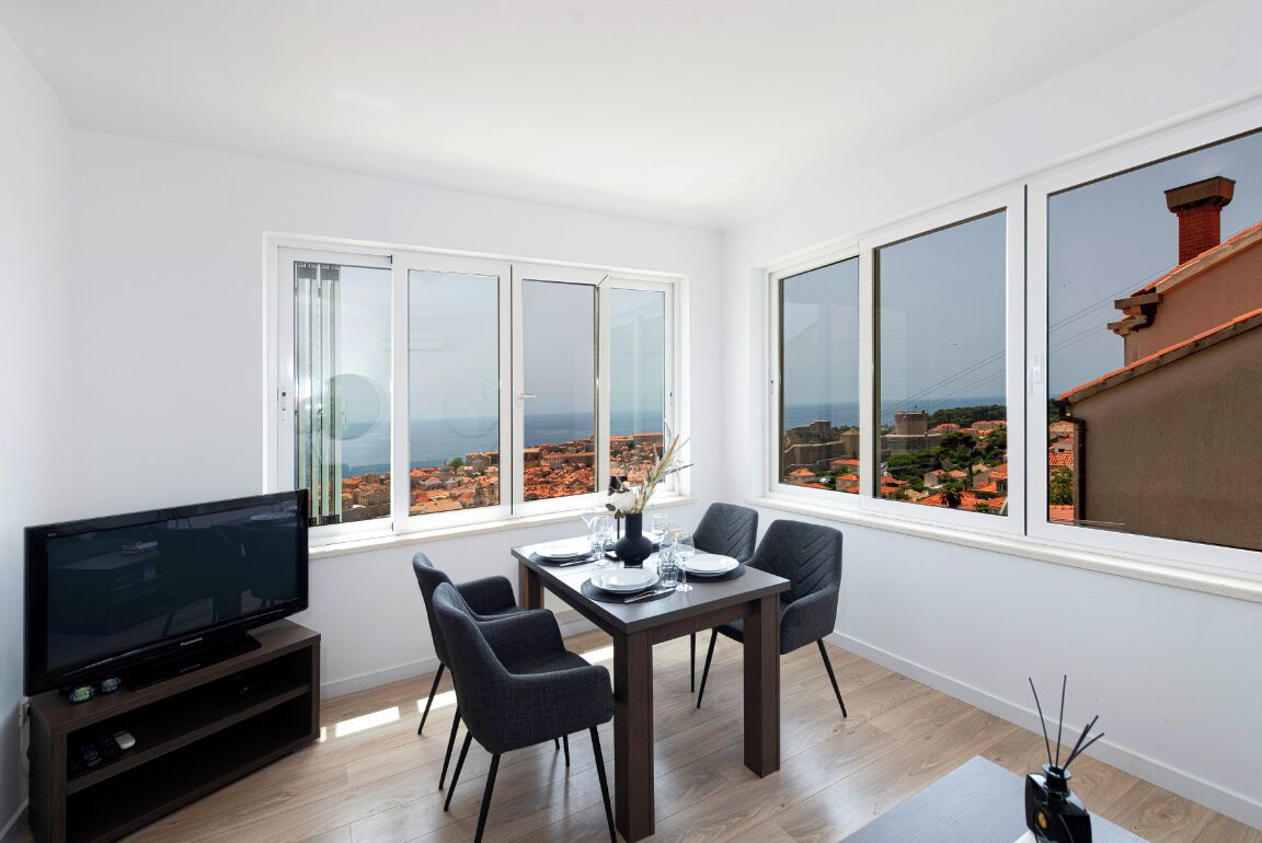 A modern living room with a flat-screen TV, dining table, and chairs.