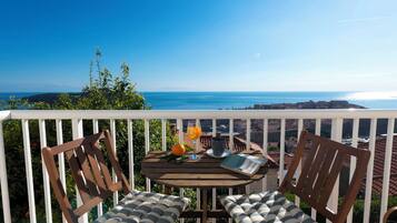 Terraza de madera con dos sillas y una mesa, con vistas a la costa.