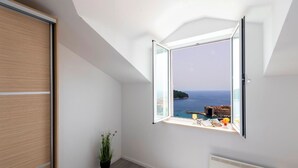 Une chambre avec un puits de lumière, une vue sur la mer, un lit, une plante et une fenêtre donnant sur une zone côtière.