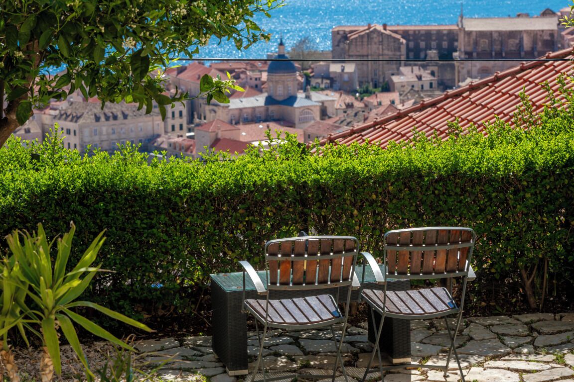 A terrace with two metal chairs and a table, overlooking a cityscape with historic buildings and a dome structure.