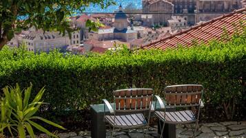 A terrace with two metal chairs and a table, overlooking a cityscape with historic buildings and a dome structure.