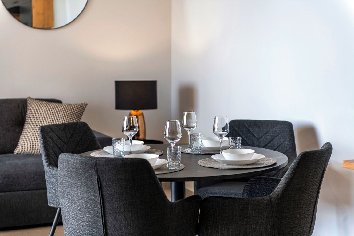 Un coin repas avec une table ronde dressée pour quatre personnes, entourée de quatre chaises.