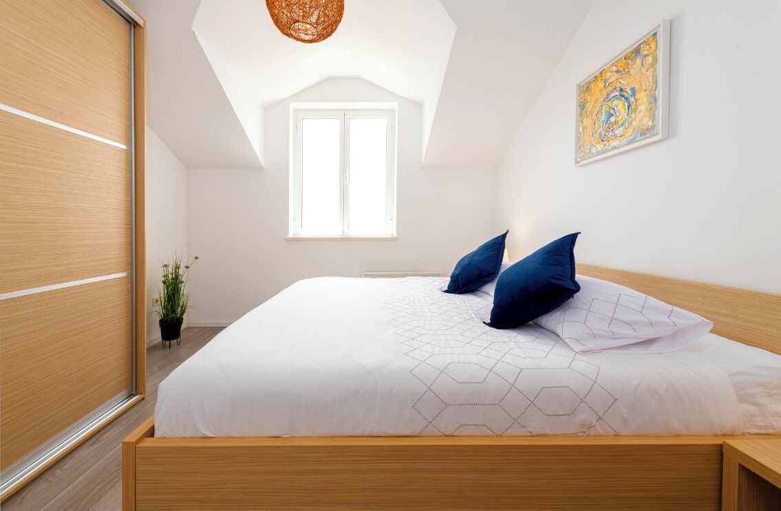 Un dormitorio moderno con una cama de madera, ropa de cama blanca y un almohadón estampado con motivos geométricos.
