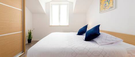 Un dormitorio moderno con una cama de madera, ropa de cama blanca y un almohadón estampado con motivos geométricos.