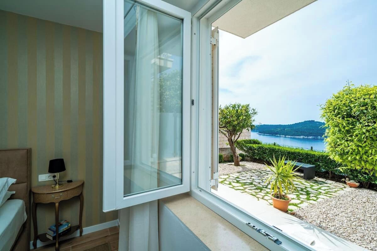 Una habitación con un ventanal grande, una cama, una mesita de noche con lámpara y vistas a un jardín y un lago.