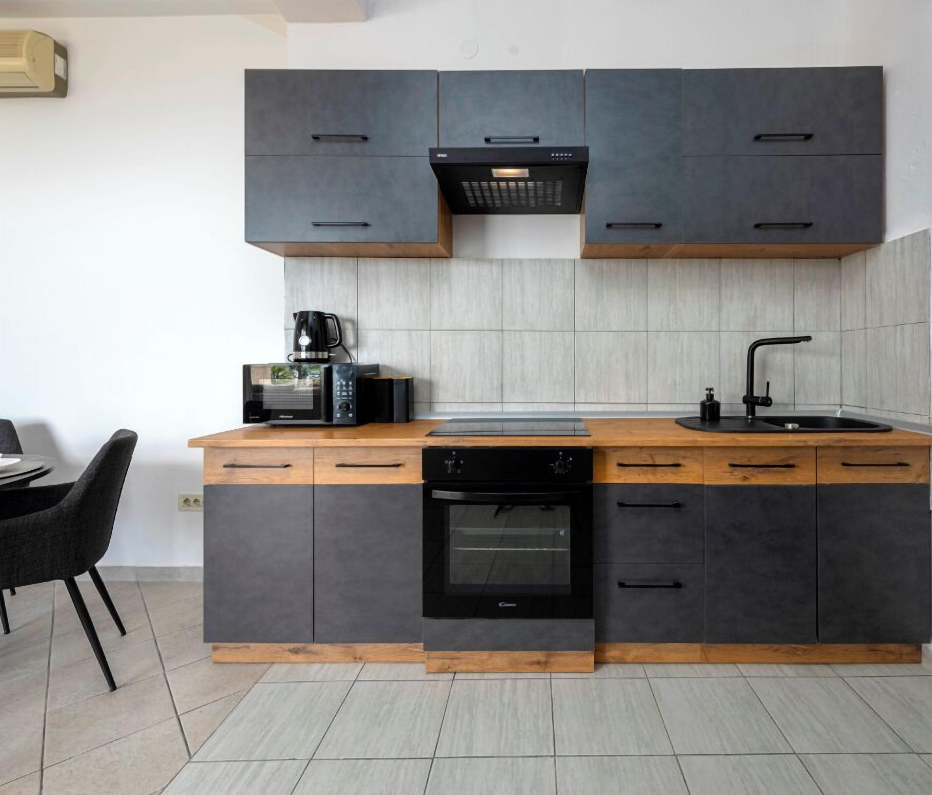 A modern kitchen with dark grey cabinets, a wooden countertop, a built-in oven, and a coffee maker.