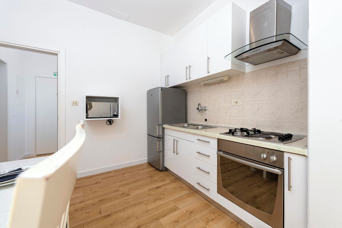 A modern kitchen with white cabinets, a stainless steel refrigerator, a built-in oven, and a gas stove.