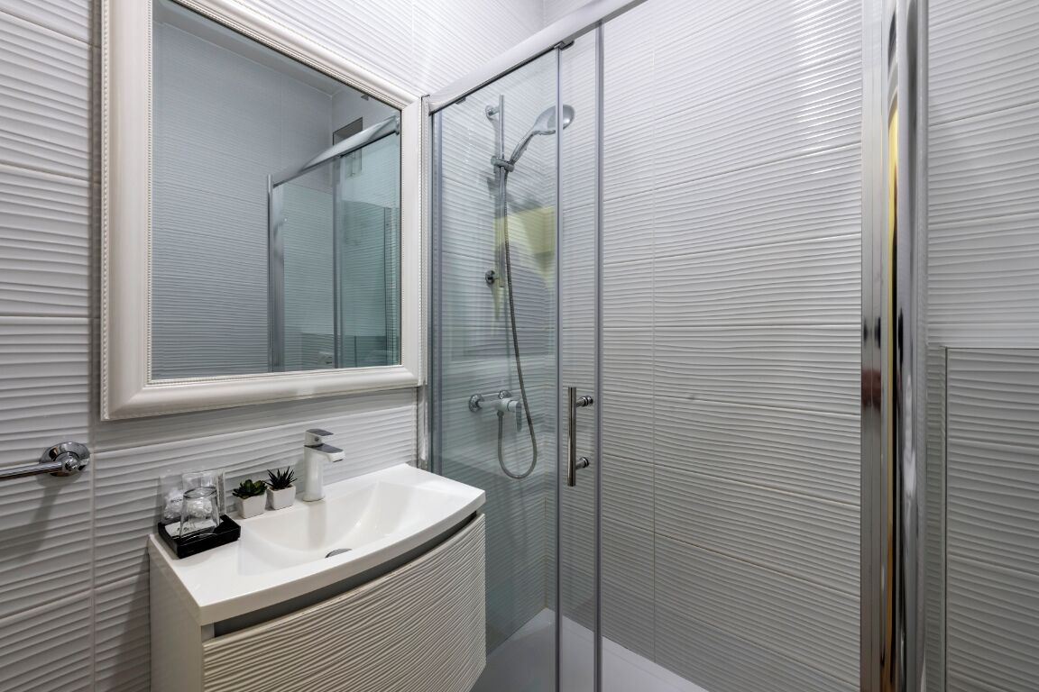 A modern bathroom with a glass-enclosed shower, a white sink, and a mirror above the sink.