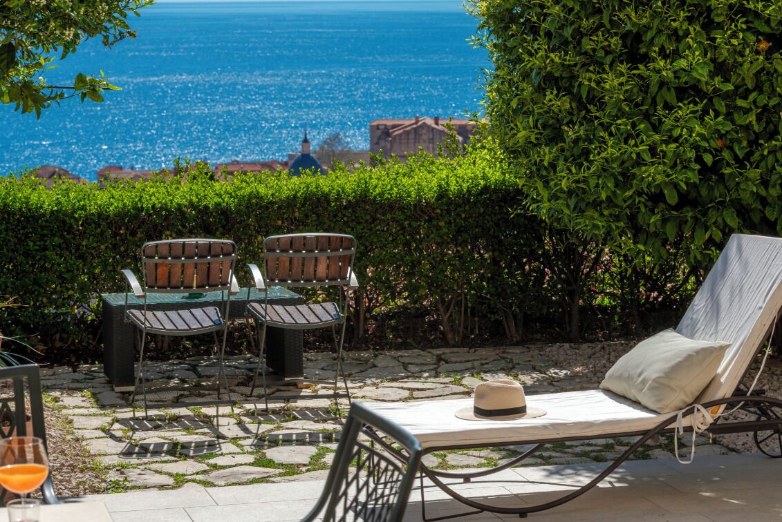 An outdoor seating area with a view of the sea, featuring a table and two chairs, and a lounge chair.