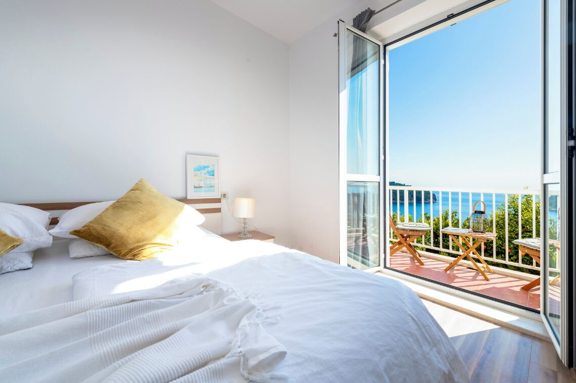 Een hotelkamer met een groot bed, een balkon met buitenmeubilair en uitzicht op zee.