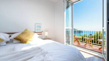 Een hotelkamer met een groot bed, een balkon met buitenmeubilair en uitzicht op zee.