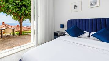 A bedroom with a large bed, a nightstand, a lamp, and a view of a tree and outdoor seating area.