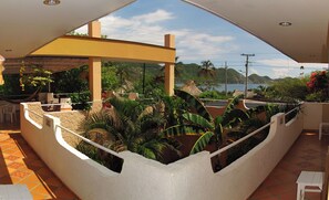 A covered outdoor area with a seating arrangement, surrounded by tropical plants and a view of the sea and hills. - Hotel Casa Dmer (Taganga)