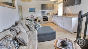 Ein modernes Wohnzimmer mit einer Couch, einem Hocker und einem Essbereich mit Stühlen und einem Tisch.