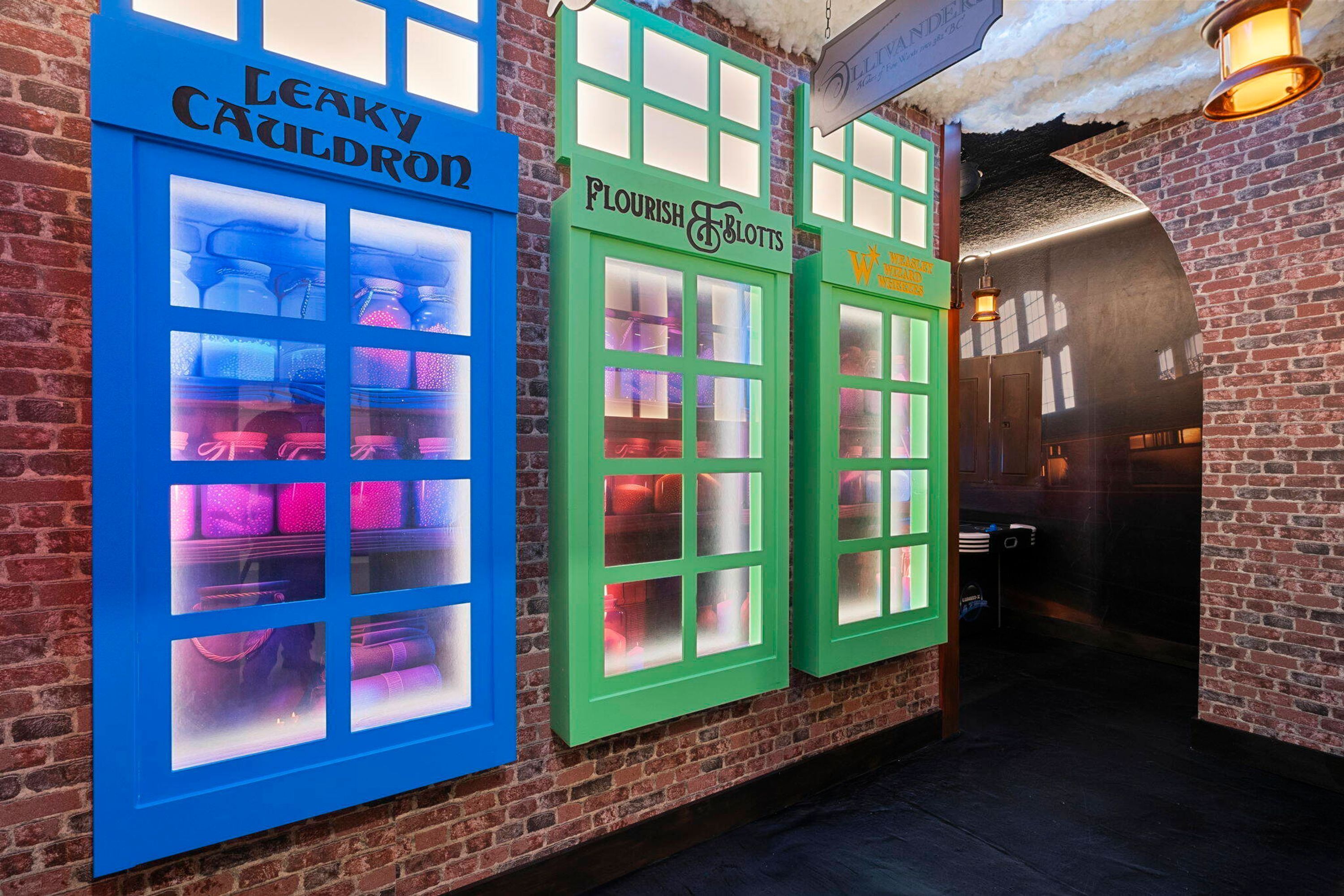 A brick wall with two storefronts, one labeled "Leaky Cauldron" and the other "Flourish & Lofts," both with illuminated windows.