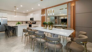 A modern kitchen with white cabinets, a central island, and a dining area with bar stools. - Incredible 10bd Summerkitchen Windsor Cay (Clermont)