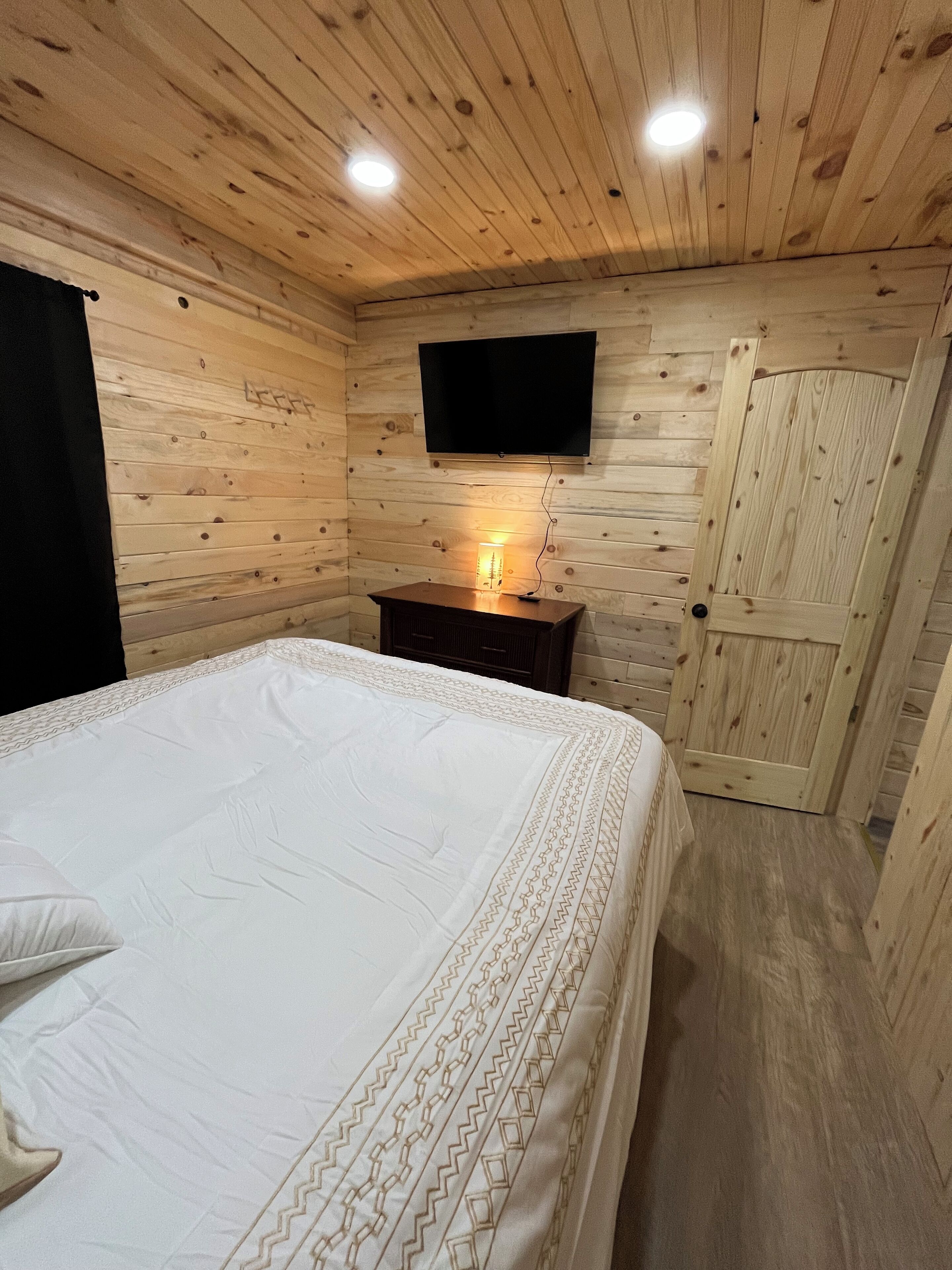 Ein Holzhütten-Zimmer mit einem Bett, einem wandmontierten Fernseher und einer Tür.
