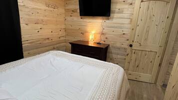 Ein Holzhütten-Zimmer mit einem Bett, einem wandmontierten Fernseher und einer Tür.