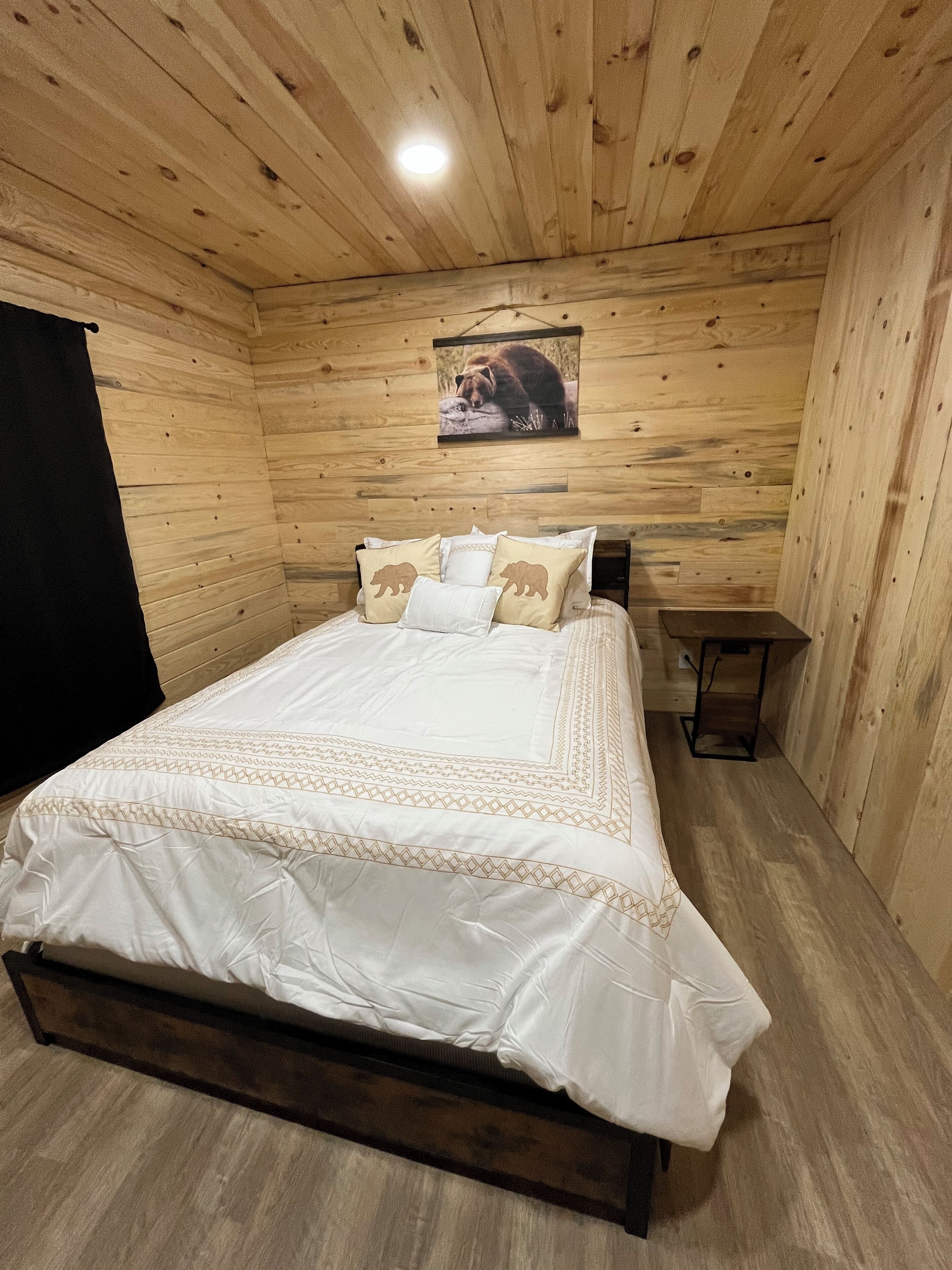 Een slaapkamer met houten lambrisering, een bed, kussens, een nachtkastje en een lijst met een afbeelding aan de muur.