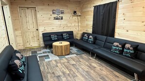 Una habitación acogedora con paredes y techo de madera, un sofá negro, una mesa de centro redonda de madera y una alfombra estampada.